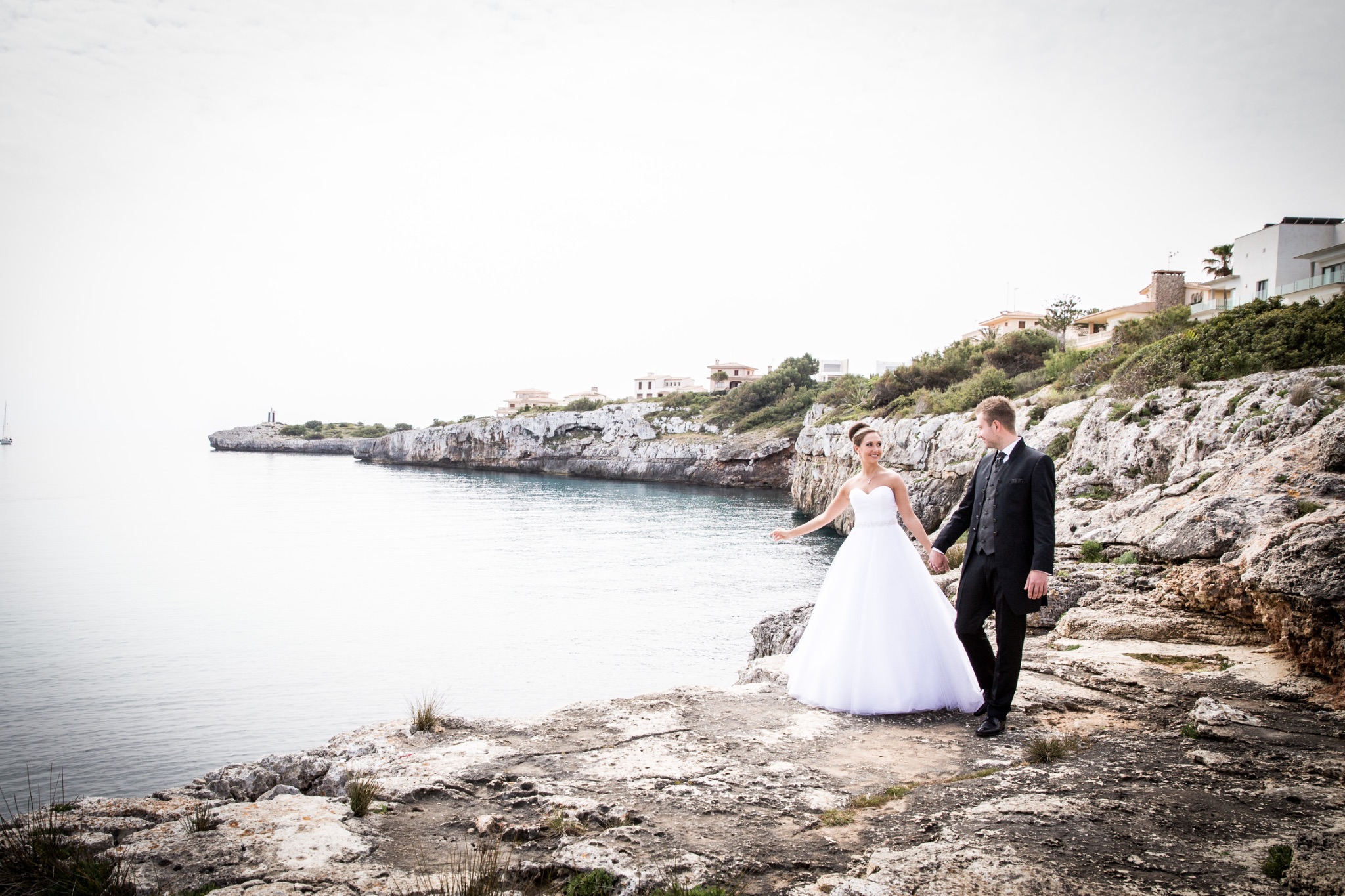 Afterwedding mallorca brautpaar geht an der wasserkante auf felsen